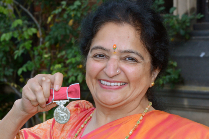 A British Empire Medal recipient wearing a sari proudly holds up her medal
