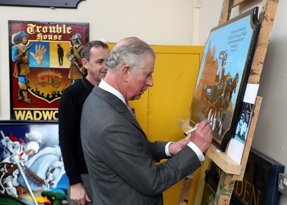 The Prince of Wales autographs a plaque during a visit to the Wadworth Brewery
