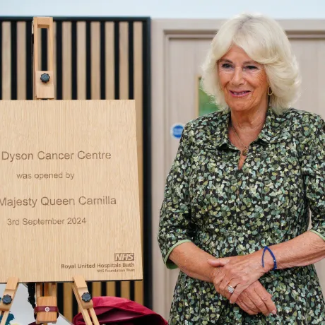 Her Majesty The Queen stands next to a plaque