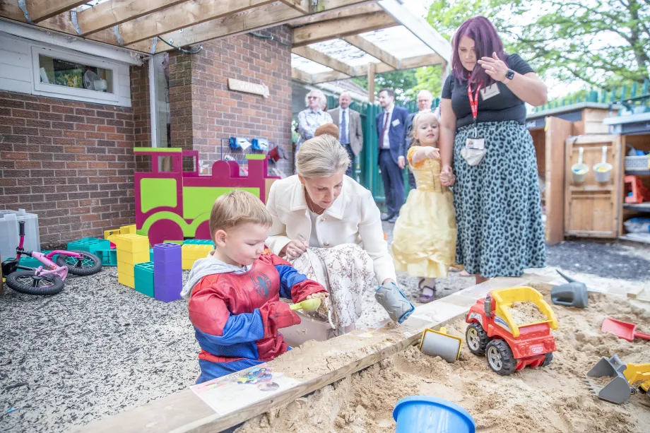 The Duchess of Edinburgh speaks to a child playing in a sand pit