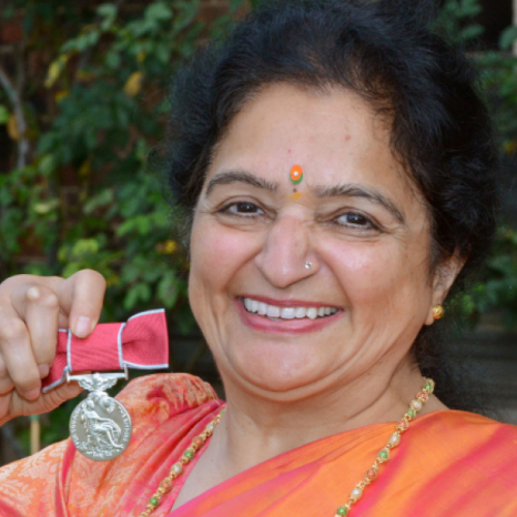 A British Empire Medal recipient wearing a sari proudly holds up her medal