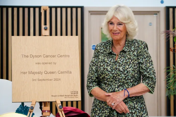 Her Majesty The Queen stands next to a plaque